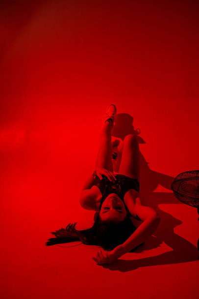 Photoshoot of a young brunette in a photo studio. Beautiful slender woman in a black top and shorts in red light. - Fotografie, Obrázek