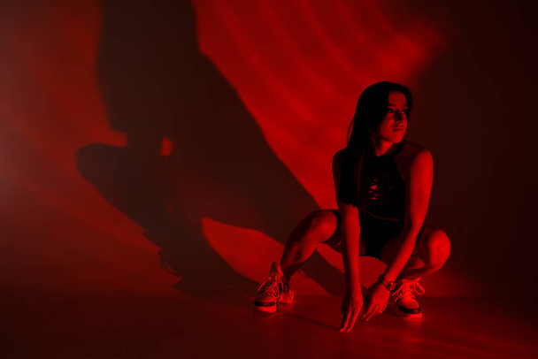 Photoshoot d'une jeune brune dans un studio photo. Belle femme élancée dans un haut noir et un short en lumière rouge. - Photo, image