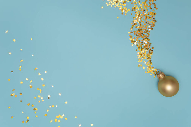 Χρυσή χριστουγεννιάτικη μπάλα με αστέρι σχήμα χρυσά κομφετί σε γαλάζιο φόντο - Φωτογραφία, εικόνα