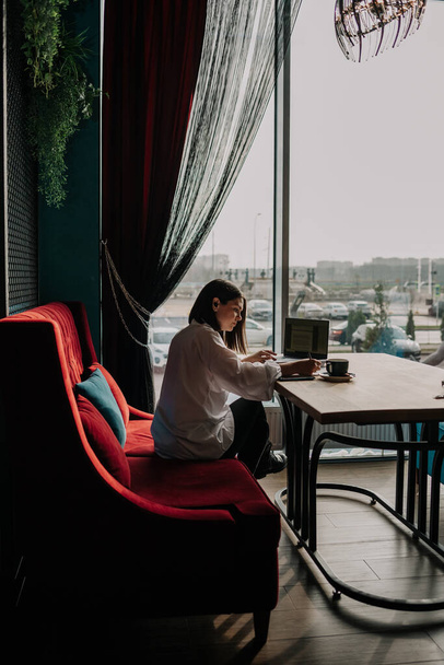 деловая женщина сидит за столом в кафе и проводит работу удаленно - Фото, изображение