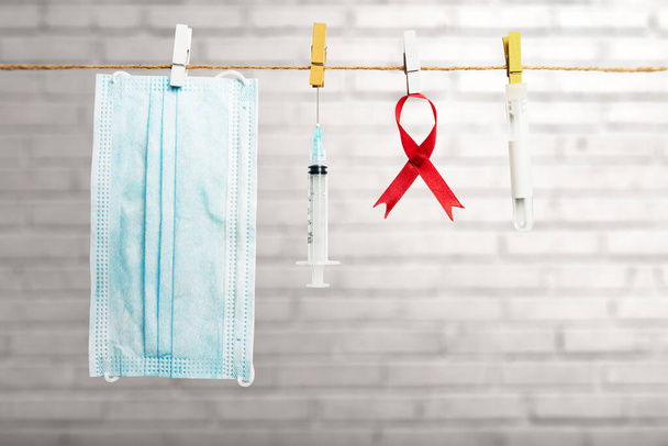 Red ribbon, syringe, and face mask hanging on the rope with brick wall background. Hiv Aids ribbon awareness - Foto, Imagem