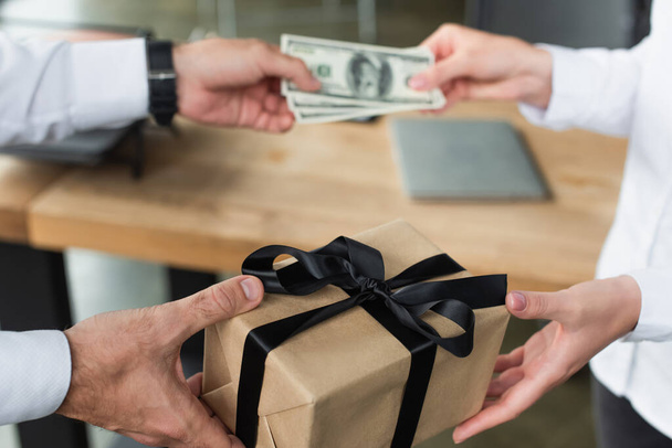 gedeeltelijke weergave van zakenman geven geschenkdoos en wazig dollars aan de vrouw, anti-corruptie concept - Foto, afbeelding