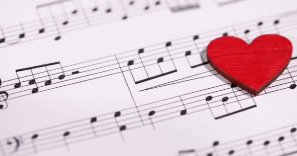 Κόκκινη ξύλινη καρδιά βρίσκεται σε μουσικές νότες αργή κίνηση 4k ταινία - Πλάνα, βίντεο