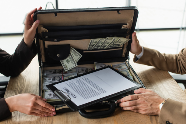partial view of business people near briefcase with dollars and contract, anti-corruption concept - 写真・画像