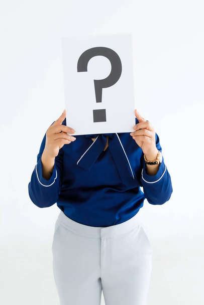 Studio shot of unidentified unrecognizable faceless female officer staff in business suit hold big question mark paper cardboard sign cover face thinking for answers on white background. - Photo, Image