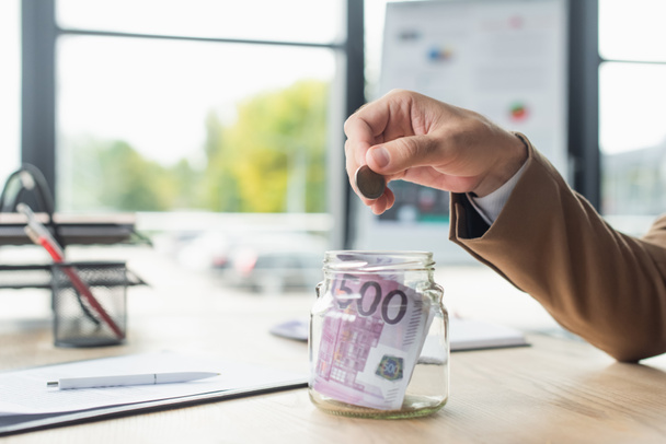 частковий вигляд бізнесмена, який тримає монету біля скляної банки з євро банкнотами в офісі, антикорупційна концепція
 - Фото, зображення