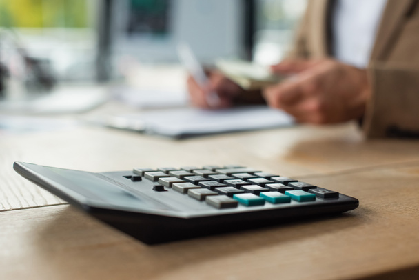 selective focus of calculator near cropped accountant counting money on blurred background, anti-corruption concept - Photo, Image