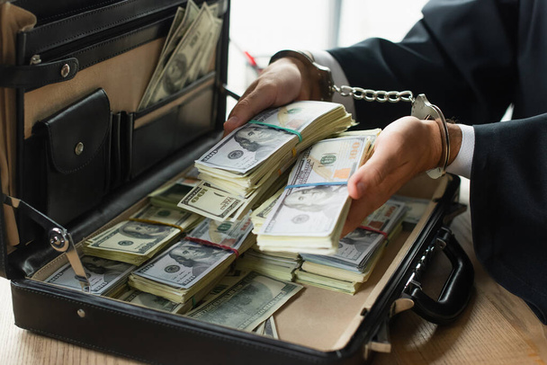vista parcial del empresario esposado sosteniendo dólares cerca del maletín, concepto anticorrupción - Foto, imagen