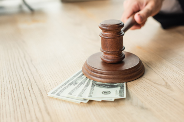 partial view of judge holding wooden gavel near dollar banknotes on desk, anti-corruption concept - Φωτογραφία, εικόνα