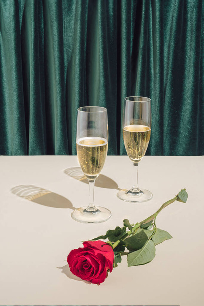 Ελάχιστη ρομαντική 2022 Νέο Έτος ή Χριστουγεννιάτικη σύνθεση κόμμα. Καλλιτεχνική κατεύθυνση με ποτήρια σαμπάνιας και κόκκινο τριαντάφυλλο. - Φωτογραφία, εικόνα