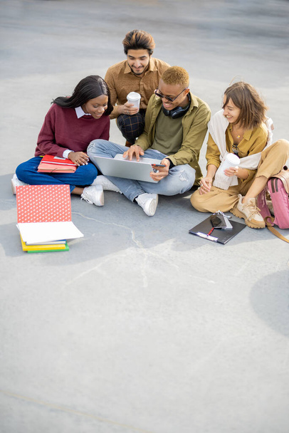 Students watching something on laptop on asphalt - Valokuva, kuva