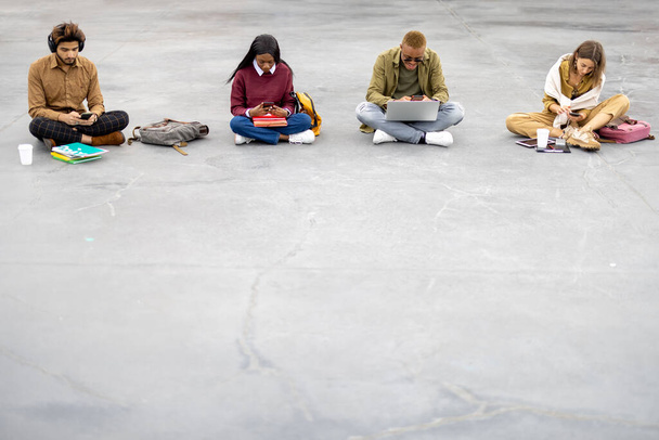 Студенты сидят и используют гаджеты на асфальте - Фото, изображение