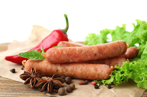 Smoked thin sausages  with lettuce salad leaves and spices on wooden cutting board, isolated on white - Фото, зображення