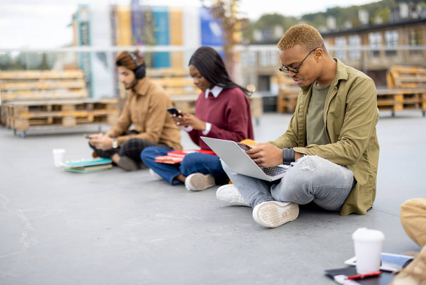 Студенти, які сидять і використовують смартфони на асфальті
 - Фото, зображення