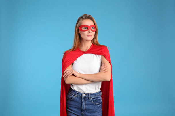 Confident woman wearing superhero cape and mask on light blue background - Foto, imagen