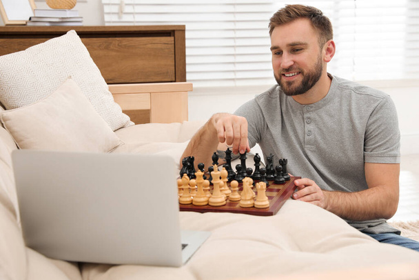 Young man playing chess with partner through online video chat at home - Фото, изображение