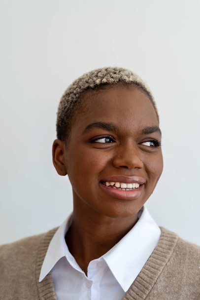 Позитивний афро-американець в стильному одязі і з пофарбованим коротким волоссям з чарівною посмішкою на білому тлі в студії - Фото, зображення