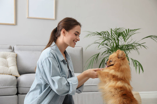 Happy young woman with cute dog in living room - Zdjęcie, obraz