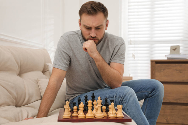 Thoughtful young man playing chess alone on sofa at home - Foto, Imagen