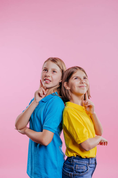Écolière portant un t-shirt bleu et jaune regardant vers le haut sur fond rose avec espace vide pour le texte - Photo, image