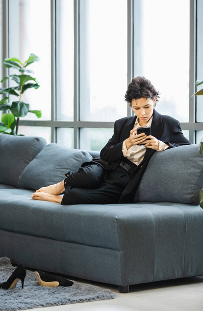 Milenyum stresi, resmi takım elbiseli Kafkasyalı genç iş kadını rahat bir koltuğa uzanmış akıllı telefon kullanarak şirket ofisinde çalışan e-posta uygulamasını kontrol ediyor.. - Fotoğraf, Görsel