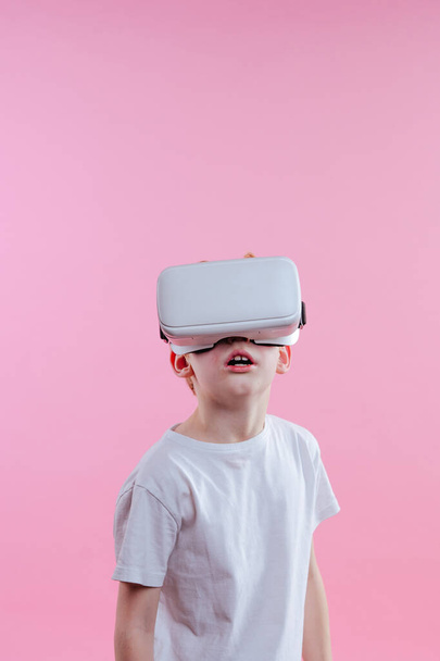 Niño adolescente con dispositivo de realidad virtual. Retrato de estudio sobre fondo rosa con espacio en blanco para texto - Foto, imagen