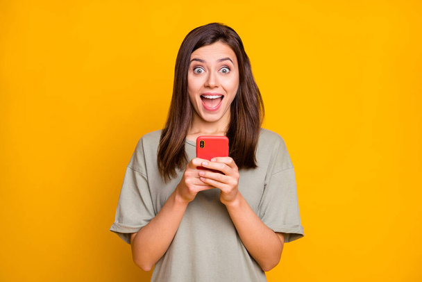 Portrait of pretty amazed cheerful brown-haired girl using device notification isolated over bright yellow color background. - Φωτογραφία, εικόνα