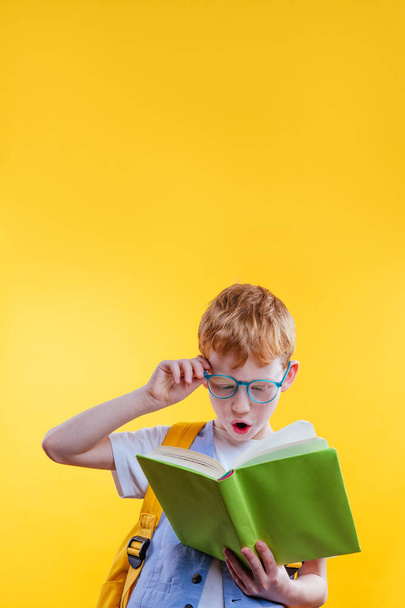 Surprised teenager boy reading book. Studio portrait on yellow background with blank space for text. - 写真・画像