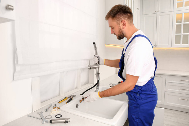 Professional plumber repairing water tap in kitchen - Фото, зображення