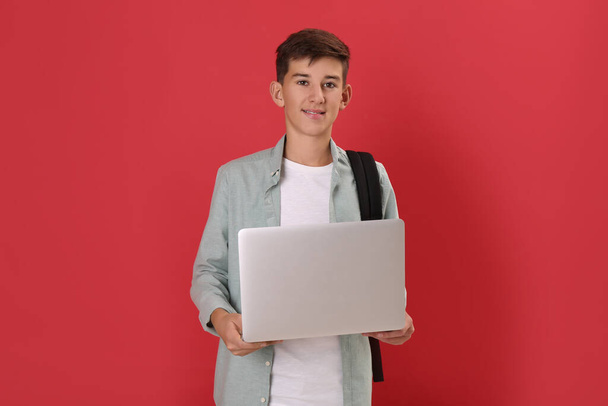 Teenage student with backpack and laptop on red background - Foto, Imagem