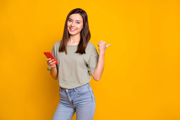 Photo of young lovely pretty happy positive cheerful smiling girl use phone point thumb copyspace isolated on yellow color background. - Фото, зображення