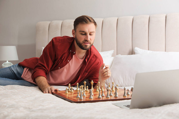 Young man playing chess with partner through online video chat on bed at home - Fotó, kép
