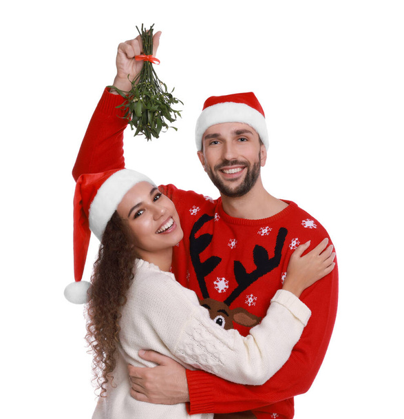 Portrait of lovely couple in Santa hats under mistletoe bunch on white background - Foto, Imagem
