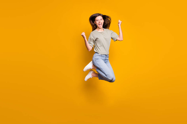Full length photo of crazy happy woman jump air up raise fists celebrate win isolated on yellow color background. - Zdjęcie, obraz