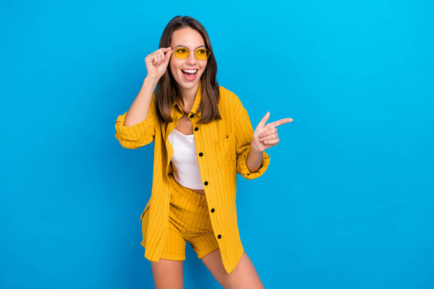 Photo of cheerful funky young woman point finger look empty space cool lady isolated on blue color background - Fotó, kép