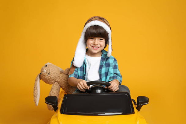 Cute little boy with toy bunny driving children's car on yellow background - Valokuva, kuva