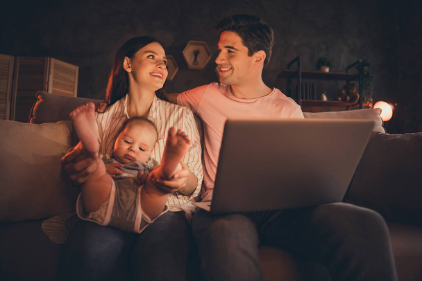 Portré vonzó teljes vidám család anyaság apaság szülői ölelés baba nézés rajzfilm otthon beltéri. - Fotó, kép