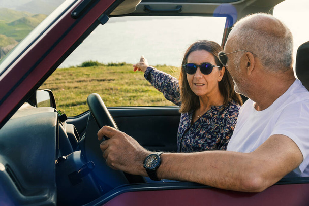 Couple âgé pointant vers l'océan et voyageant à travers la côte dans leur voiture convertible 4x4 - Photo, image