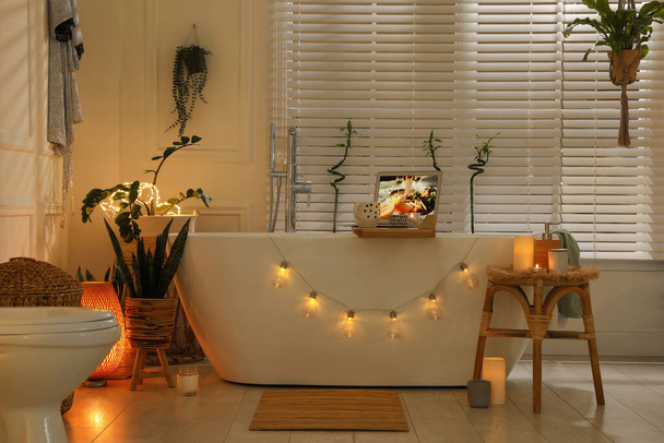 Stylish bathroom interior with green houseplants and string lights. Idea for design - 写真・画像
