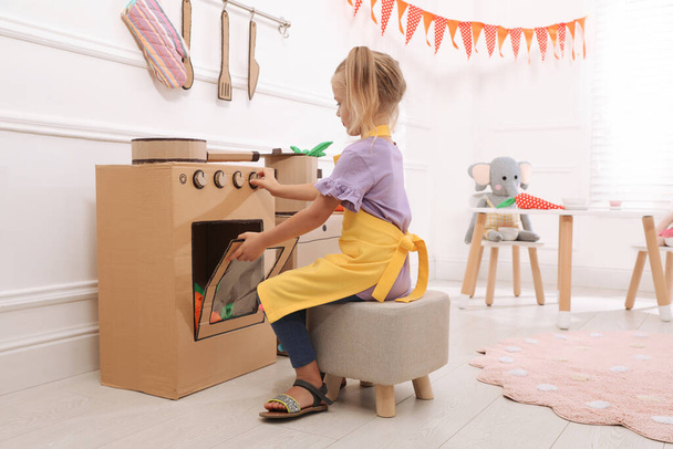 Little girl playing with toy cardboard oven at home - Φωτογραφία, εικόνα
