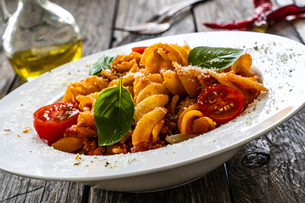 Fusilli mit Hackfleisch, Tomatensauce, Parmesan und Basilikum auf Holztisch serviert  - Foto, Bild