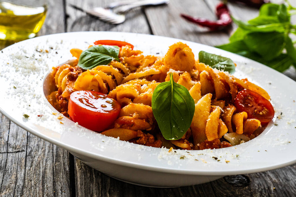Pasta with minced meat, tomato sauce, parmesan cheese and basil served on wooden table  - Fotoğraf, Görsel