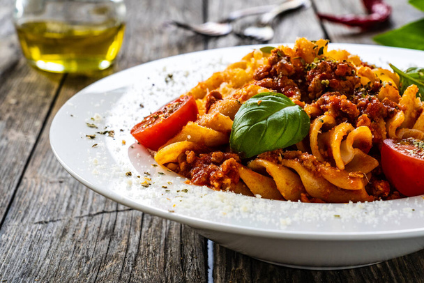 Fusilli with minced meat, tomato sauce, parmesan cheese and basil served on wooden table  - Foto, Bild