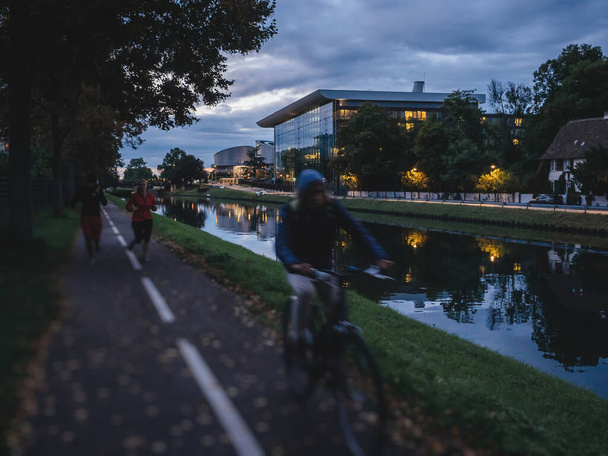 Людина сілует їде на велосипеді біля річки Ілл і будівлі Агори. - Фото, зображення