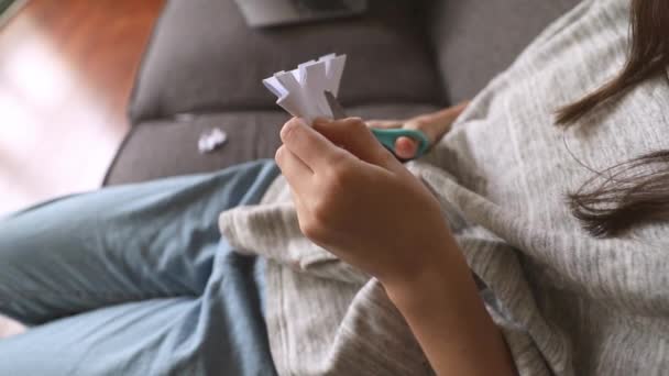 niña cortando un copo de nieve de papel blanco con tijeras en casa, educación temprana, elaboración y concepto de arte - Metraje, vídeo