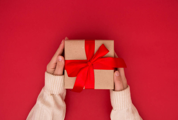 Female hands hold a gift box on a red background, copy space. Gifts and presents concepts. View from above. - Photo, Image