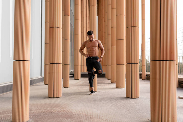 sin camisa fitness hombre fuerte está descansando contra una columna después de su entrenamiento de calistenia al aire libre - Foto, Imagen