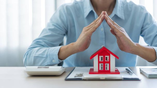 Le concept immobilier l'agent immobilier présentant son travail envers son client en mettant le modèle de maison rouge devant lui, levant les mains et mettant sa main ensemble. - Photo, image