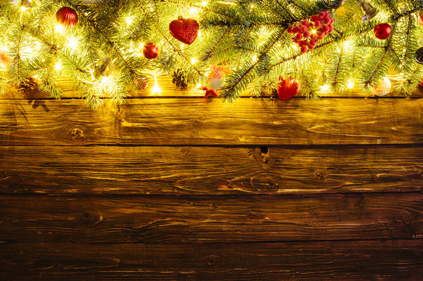 Blurred Christmas background, with fir branches, fairy lights and christmas decorations on wooden plank - Fotografie, Obrázek