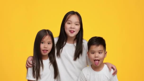 Весёлые японские братья и сёстры с веселым гримасом показывают языки, жёлтый фон - Кадры, видео